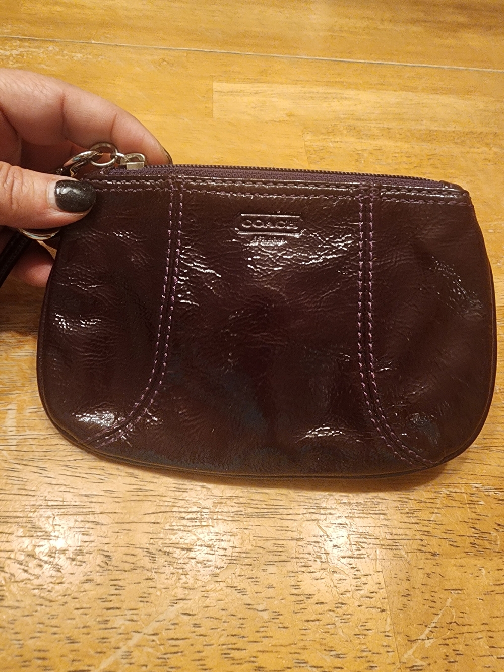 plum patent leather Coach wristlet with an embossed front logo and silver-tone